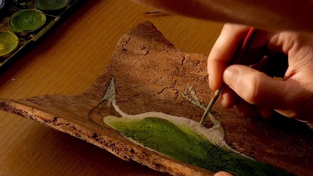 closeup of a female artist painting a green woodpecker on a piece of spruce wood