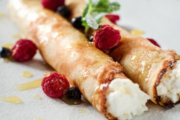 Sweet crepe with cottage cheese and berriesm closeup. Restaurant serving of healthy morning breakfast. Homemade rolled pancake dessert with raspberries on white plate.