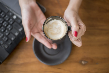 close up of woman hand holding hot coffee cup on wooden table