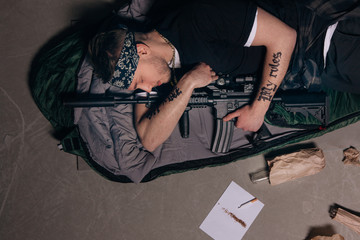 Gangster sleep with rifle. Gang wars concept. Cigarette, alcohol, weapon top view. Careless lifestyle, social problem, negative addiction concept