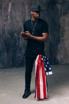 Afro american man with usa flag as accessory on dark background. Casual guy ready to celebrate. Patriot, national event celebration, independence day, pride, immigration, us citizenship concept