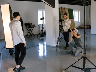 Fototapeta na wymiar Professional photo and video production team work together. Two photographers taking shots of male model in studio. Fashion photoshooting backstage