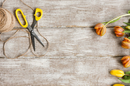 Tulips, scissors and rope on wooden background. Top view on workplace with diy tools and flowers. Decoration equipment, florist, decorator, handmade concept.