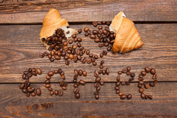 Fototapeta na wymiar Roasted coffee beans in croissant on wooden background. Closeup of seed filling on dark brown table. Top view. Extra energy concept