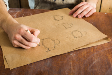 pottery manufacture, artisan tools, ceramics art concept - closeup on young man's hands and working drawing of earthenware, a male ceramist sitting at a Desk and working on the design project