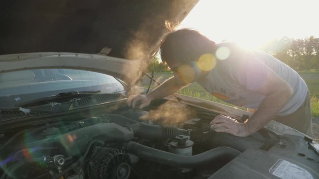 Smoke coming out of a vehicle, man trying to take a look on the side of the road.