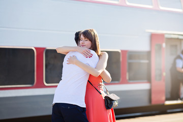 Young caucasian couple standing at the train station, hugging for goodbye