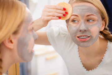 Woman removing mud facial mask with sponge