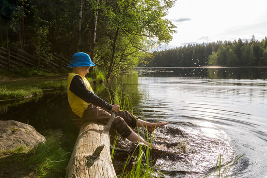 The boy splashes by  his feet in the lake, summer in Finland