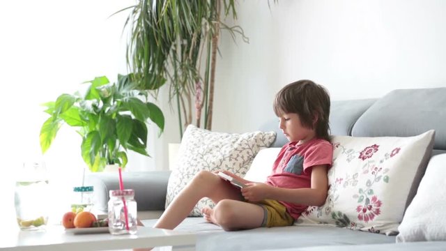 Cute little child, reading a book with pictures at home, sitting on the sofa