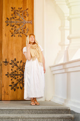 Girl in white dress and scarf on the background of wrought wooden gates and white columns