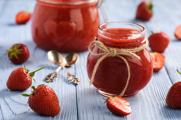 Strawberry jam in glass jar on wooden background.