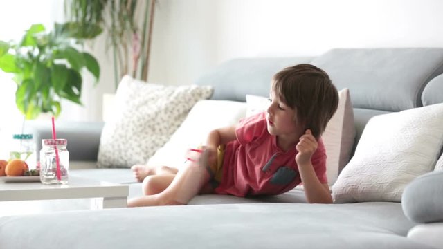 Cute little child, reading a book with pictures at home, sitting on the sofa