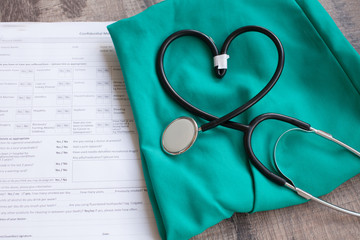 A stethoscope shaping a heart and a clipboard on a medical uniform, closeup