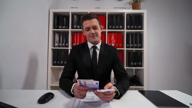4k uhd POV handsome business man in black suit and tie counting euro with smile. The promise that the work and servise will be done. Hide money in pocket. Office indoor.
