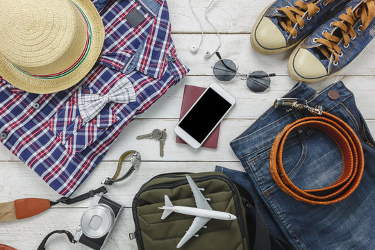 Top view accessories to travel with man clothing concept. shirt,jean,mobile phone ,headphone on wooden background.passport,key,sunglasses and hat on wood table.