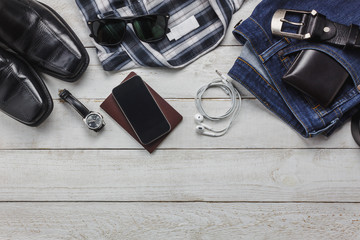 Top view accessories to travel with man clothing concept. shirt,jean,mobile phone on wooden background.watch,sunglasses and shoes on wood table.