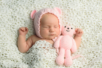Fototapeta na wymiar Sweet dreams of a newborn baby girl in a knitted hat and toy sleeping her side