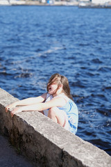 Fototapeta na wymiar Portrait of a girl sitting on the quay wall in the port