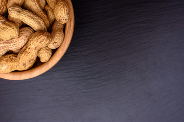 Peanuts lie in a wooden cup on a black stone board in the form of a frame, space for text