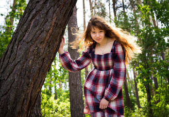 Beautiful red-haired girl sitting under a tree. The wind develops her hair. It is beautifully illuminated by the sun behind.