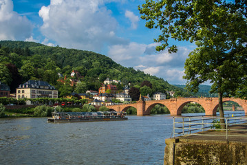 HEIDELBERG, GERMANY - JUNE 4, 2017: River Nickar embankment, touristic boat, Old bridge and a hill at the background on sunny summer evening.