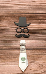 Happy fathers day sticker, hat, glasses, black mustache, tie from dollar bills on a background of wooden texture. Hipsters objects. Father's Day is a holiday