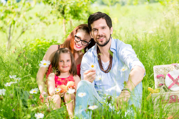 Fototapeta premium Family having picnic on meadow with healthy fruit, looking into camera