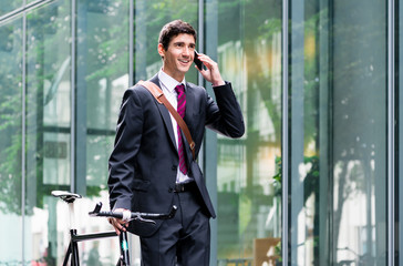 Young confident man  wearing business suit while talking on mobile phone after bike commuting