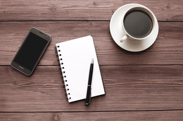 Smartphone cup coffee notepad ballpoint pen on the desktop made of wood.