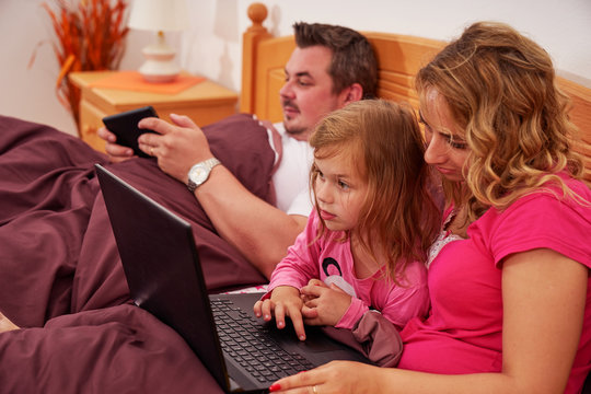 A family using digital devices in bed in the morning