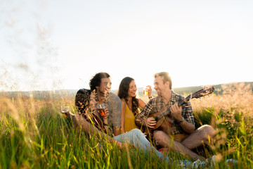 Friends sitting together in grass playing guitar and chilling