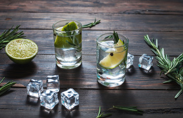 Alcoholic drink - gin tonic cocktail - with lime, rosemary and ice on rustic wooden table