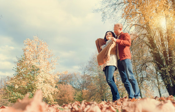 Man covers his wife shoulders with warm shawl in autumn park