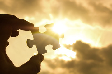 hand trying to connect couple puzzle piece with sunset background. Jigsaw alone wooden puzzle...