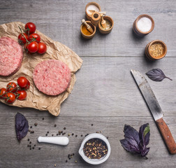 raw cutlet for burgers, with cherry tomatoes and herbs on a packaging paper with unground black pepper, knife for meat on wooden rustic background top view close up place for text,frame