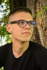 Portrait of young and smiling cute man with glasses in park, teenager