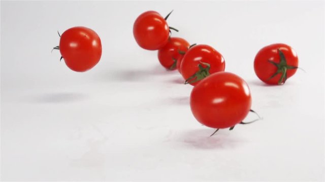 Many Fresh red tasty tomatoes with green tail falling on white background in super slow motion rapid high speed camera macro. Bouncing on wet surface.
