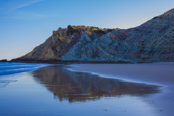 Beautiful sandy beach on the coast of Portugal at sunset, the rock is reflected in the wet sand