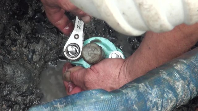 A worker is putting a clamp on a pipe is broken. Water leak on a street in the city of Taipei, Taiwan.