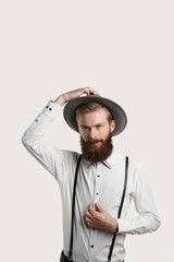 Italian farmer worker studio shot. Stylish beard man in white shirt and grey hat. True hipster look into the camera. Clan shaved temples and moustaches looking serious and brutal with long facial hear