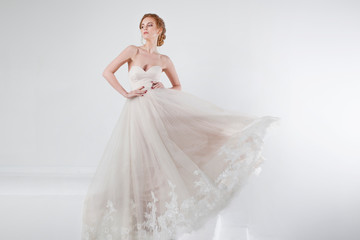 Fototapeta premium Portrait of a beautiful girl in a wedding dress. Bride in luxurious dress on a white background, hands on waist