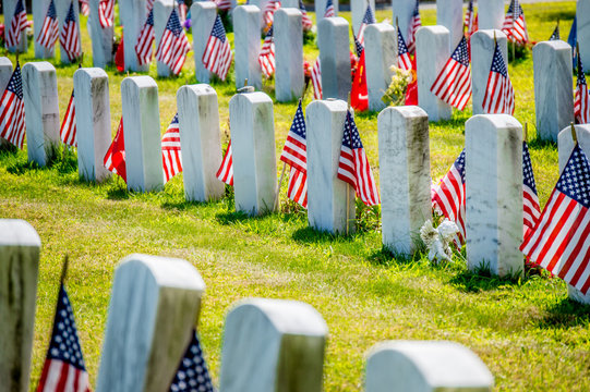 rows of grave markers with American flags in military cemetery