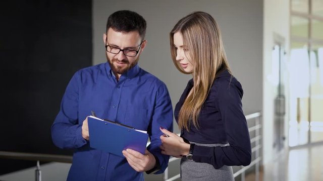 Inside the office building. The boss gives instructions to the manager. A man shows information on a clipboard.