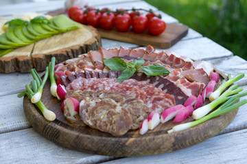 Food tray with delicious salami, pieces of sliced ham, sausage, tomatoes, salad and vegetable - Meat platter with selection - Cutting sausage and cured meat on a celebratory table.