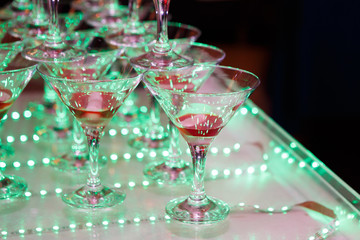 Glasses of bubbling champagne on colorful table. Banquet with alcohol lit with colored lights. Luxury party in color.