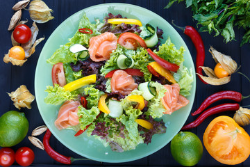 Fresh vegetable salad with salmon on green plate, decorated with physalis, chili peppers, lime, herbs and spices