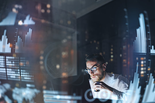 Concept of digital diagram,graph interfaces,virtual screen,connections icon.Young finance analist working at modern office.Man using contemporary laptop at night,blurred background.Horizontal.