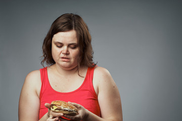 Hungry woman with a hamburger looking at a hamburger on a gray background studio
