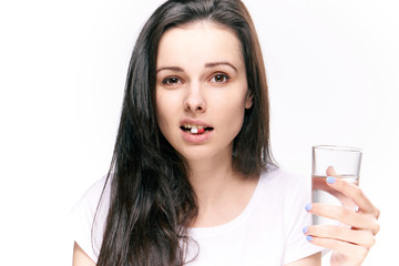 Woman with a pill in her mouth and a glass of water on an isolated background